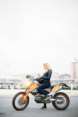 Naklejka na ściany i meble Young woman at motorcycle using mobile phone