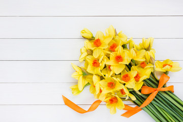 Bouquet of fresh spring narcissus decorated with ribbon on white wooden table. Top view, copy space