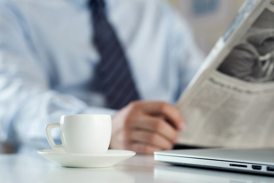 Cup of morning coffee on worktable with businessman reading news
