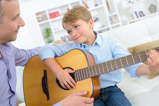 Young boy playing guitar to father