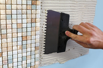 Repair in the apartment: installing the mosaic tile on the wall.