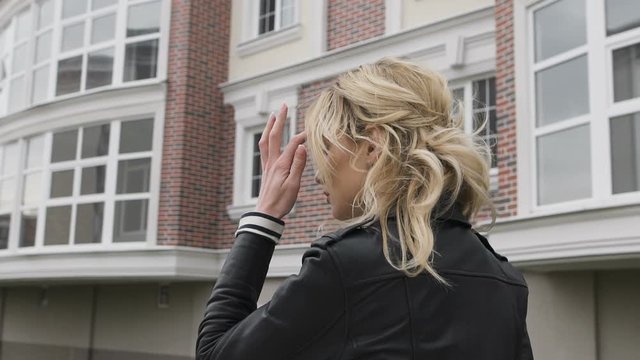 Young woman walking on the street. Self-confident blonde striding purposefully down the street. Black leather jacket