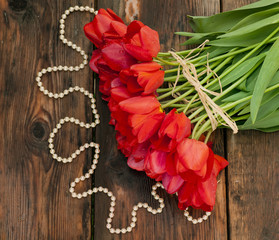 Beautiful red tulips on wooden background with white pearls