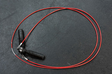Red jump rope with black handles on a black gym floor
 - obrazy, fototapety, plakaty