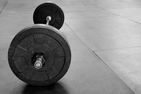 Clean black and white image of a barbell on a gym floor

