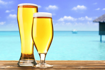 Glasses of cold fresh beer on table, on sea or ocean background