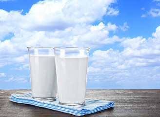 Glasses of milk on wooden table against blue sky background