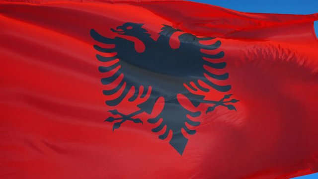 Albania flag waving in slow motion against clean blue sky, seamlessly looped, close up, isolated on alpha channel with black and white luminance matte, perfect for film, news, digital composition