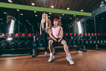 Fototapeta na wymiar sport, bodybuilding, weightlifting, lifestyle and people concept - Young beautiful couple in stylish clothes sitting a gym near the dumbbells