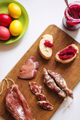 Top view vertical image of various meats on serving board. Ham, pork, beef, red wine, easter eggs and homemade bread with beetroot-horseradish spread. Preparing for dinner to celebrate Easter