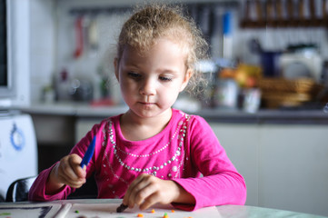 Girl sits at a table in the kitchen. She cuts a knife plasticine