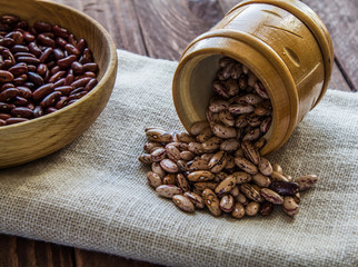 Raw beans in a wooden plate and a wooden pot on a napkin
