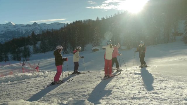 Young teenage girls finish with ski preparation and leave with instructor on the ski slopes on sunny winter morning.
