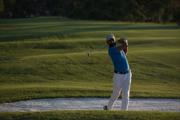 golfer hitting a sand bunker shot on sunset
