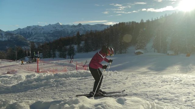 A young woman is preparing for skiing and start to ski down the ski slopes on sunny winter morning.
