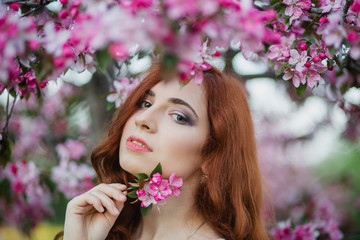 Naklejka premium Closeup portrait of beautiful female hold blossom branch in fresh pink floral garden, warm sunset light, spring nature, vacation and leisure concept