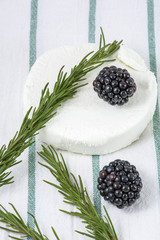 Two blackberries are on the goat cheese with rosemary on the white towel with green stripes