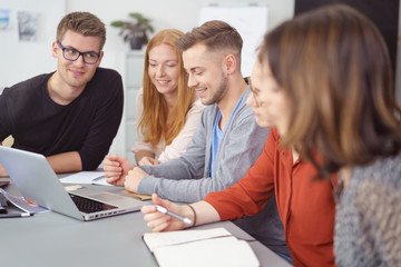 gruppe junger leute sitzt am schreibtisch und schaut gemeinsam auf laptop