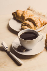 Croissants with cup of coffee on wooden background. Toned image.