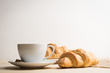 Croissants with cup of coffee on wooden background