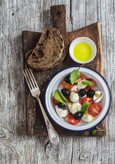 Fresh salad with mozzarella, tomatoes and olives, rye bread and olive oil on wooden rustic board