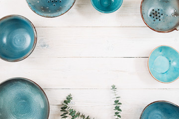 Many turquoise clay empty plates and free space in center on a white wooden background. Flat lay of...