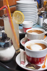 Two red and white espresso - macchiato cups with saucer, sugar dispenser and lemonade on a tray on...