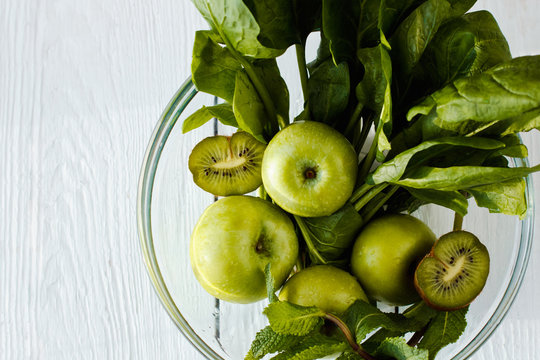 The concept of a healthy and healthy meal: fresh green apples, spinach, mint and kiwifruit in a glass bowl on wooden background