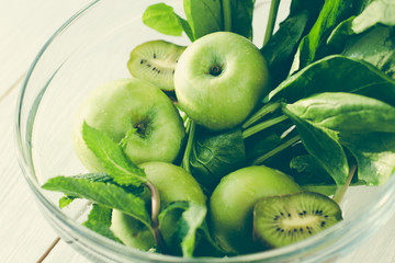 The concept of a healthy and healthy meal: fresh green apples, spinach, mint and kiwifruit in a glass bowl on wooden background