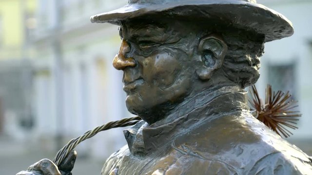 A statue of a chimney sweeper in the streets. The old man statue is found in the middle of the street