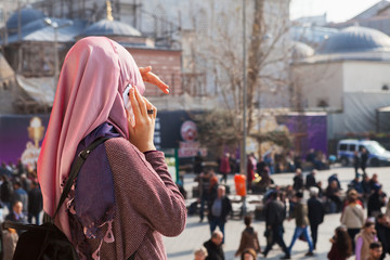 Young woman stands in front of the New Mosque ( Yeni Cami ) and speaks on the mobile phone - obrazy, fototapety, plakaty