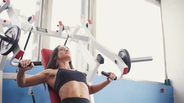 young woman flexing muscles on cable gym machine.