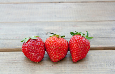 Three strawberries close up on the wooden floor.