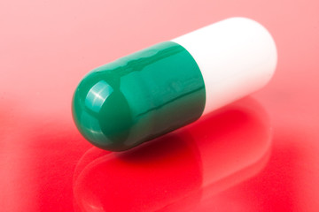 one green white pills on a red background