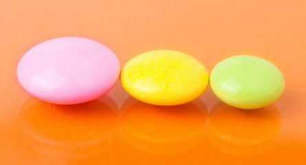 Three multicolored pills on orange background close up macro