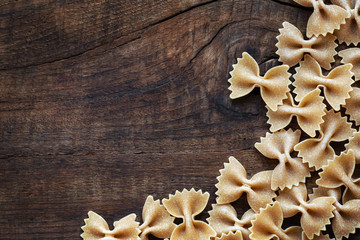Obraz na płótnie Canvas Wholemeal farfalle pasta on dark rustic wooden background with copyspace your text. Overhead view