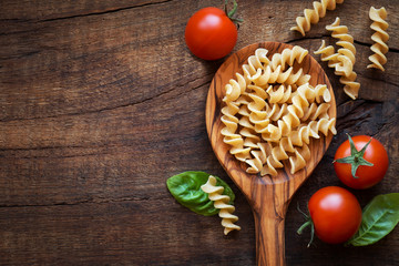 Italian cuisine concept - Wholemeal farfalle pasta in wooden spoon with fresh basil and tomatoes od dark rustic wooden background . With copy space for your text