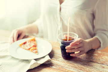 Midsection of woman with pizza slice and cola soda drink