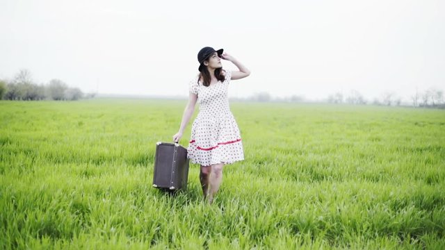 woman dressed in retro style carries luggage through the green field slow motion 