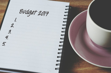Budget list for 2017 on notepad with cup of coffee, retro style background.
