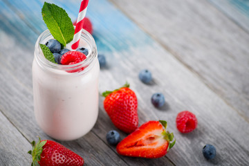 Jar with drinking yogurt, berries and straw on wooden table