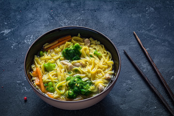 Asian noodle soup Ramen with vegetables and pork in bowl and chopsticks on textured background