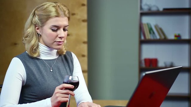 Surprised woman reading latest news on the internet, drinking red wine