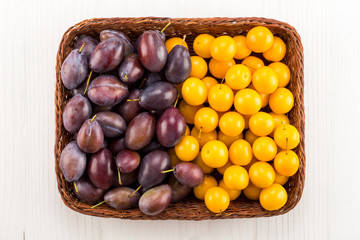 Different kinds of plums in basket on white wooden surface. Top view