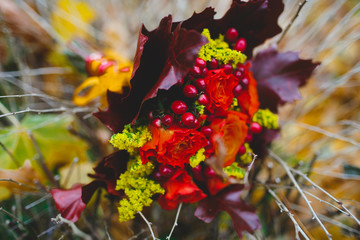 Autumn wedding bouquet of maple leaves and berries on the background of withered grass