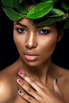 Beautiful woman portrait on black background. Young afro girl posing with green leaves. Gorgeous make up. Pure skin