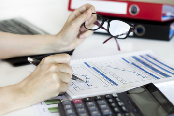 Businesswoman analyzing graphic and using calculator in the office