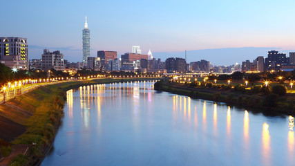 Naklejka premium Beautiful riverside scenery of busy Taipei City with view Taipei 101 Tower, Keelung River and downtown area at dusk ~ A Blue and Gloomy evening in Taipei