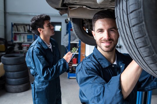 Mechanic fixing a wheel while a colleague preparing a check list
