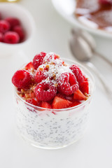 Homemade fresh chia pudding with yogurt, strawberry, raspberry, nuts and coconut in a glass on a white table, closeup